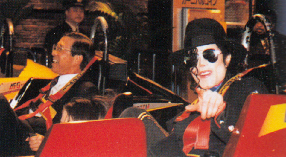 Colour photo of Michael Jackson playing Powersled at Joypolis, pointing at the camera and wearing his distinctive hat and sunglasses