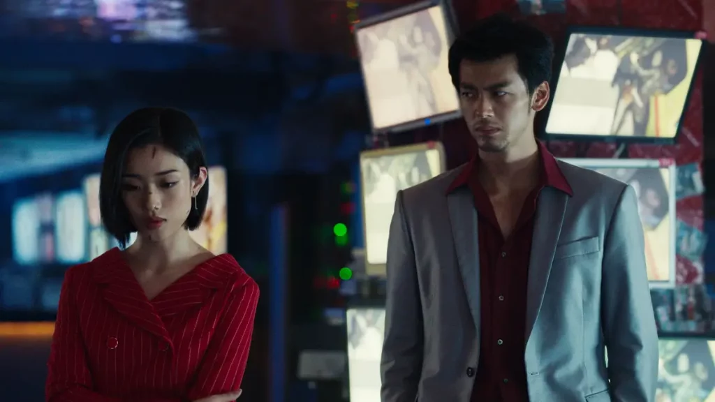 Ryoma Takeuchi looks the part dressed in Kiryu Kazuma's iconic grey suiit and red shirt. Standing next to Yuumi Kawai's Yumi dressed in a red stripy jacket and standing in front of a bank of monitors